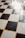 A checkered floor pattern composed of alternating black and white tiles, with a slightly worn and reflective surface. The grout between the tiles is yellowish in color, contributing to a nostalgic or vintage appearance.