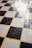 A checkered floor pattern composed of alternating black and white tiles, with a slightly worn and reflective surface. The grout between the tiles is yellowish in color, contributing to a nostalgic or vintage appearance.