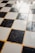 A checkered floor pattern composed of alternating black and white tiles, with a slightly worn and reflective surface. The grout between the tiles is yellowish in color, contributing to a nostalgic or vintage appearance.