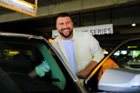 A friendly driver greeting a smiling passenger with luggage near the airport entrance.