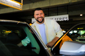 A friendly driver greeting a smiling passenger with luggage near the airport entrance.