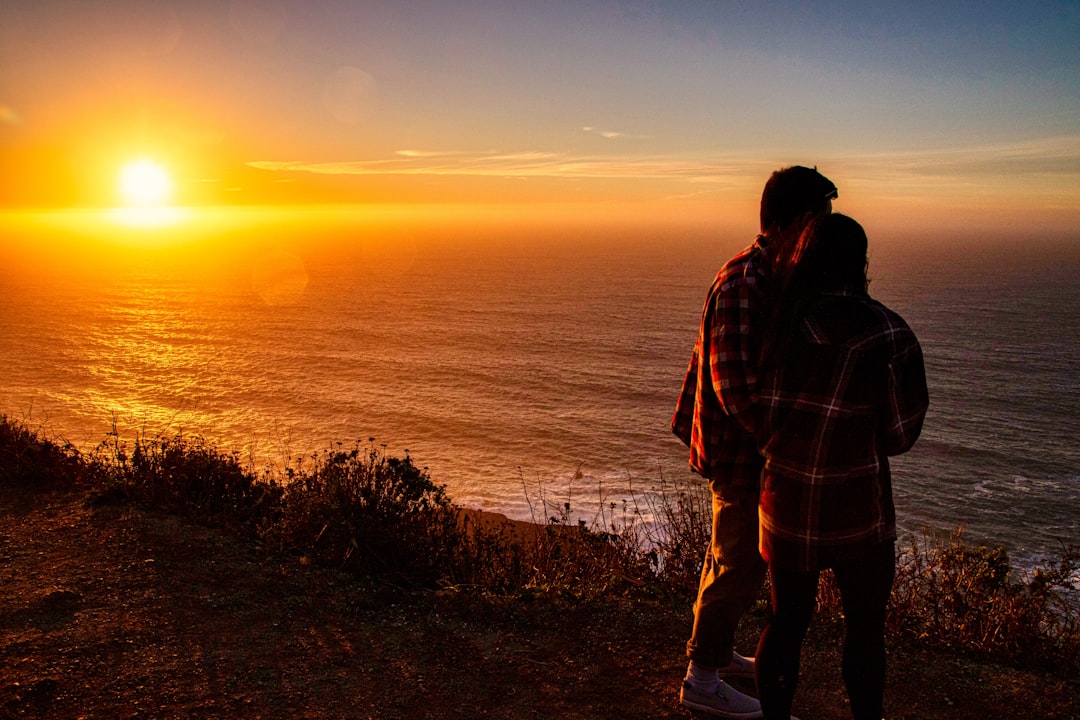 man and woman standing on island facing the ocean during golden hour