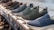 A row of slip-on shoes is neatly arranged on a white shelf, showcasing various designs and colors including blue, black, and dark grey. The shoes have a casual style and appear to be made of breathable fabric with textured patterns. The display creates a sense of order and organization within a retail setting.