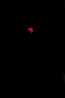 A dark background with a partially visible red circular shape, resembling a solar eclipse. The red object has a curved section covered, creating an appearance of intense contrast against the black surroundings.