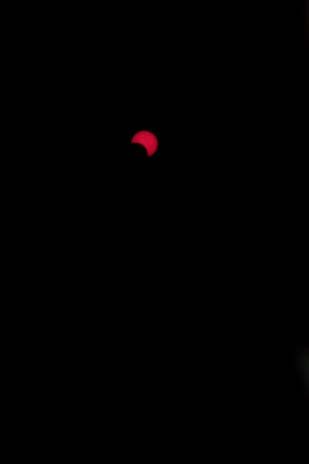 A dark background with a partially visible red circular shape, resembling a solar eclipse. The red object has a curved section covered, creating an appearance of intense contrast against the black surroundings.