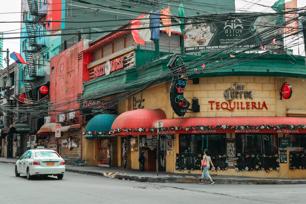 Bâtiment de Tequileria près d’une berline blanche sur la route et d’une femme marchant pendant la journée