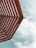 A perspective of a wooden pergola with slatted beams set against a partly cloudy sky.