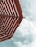 A perspective of a wooden pergola with slatted beams set against a partly cloudy sky.
