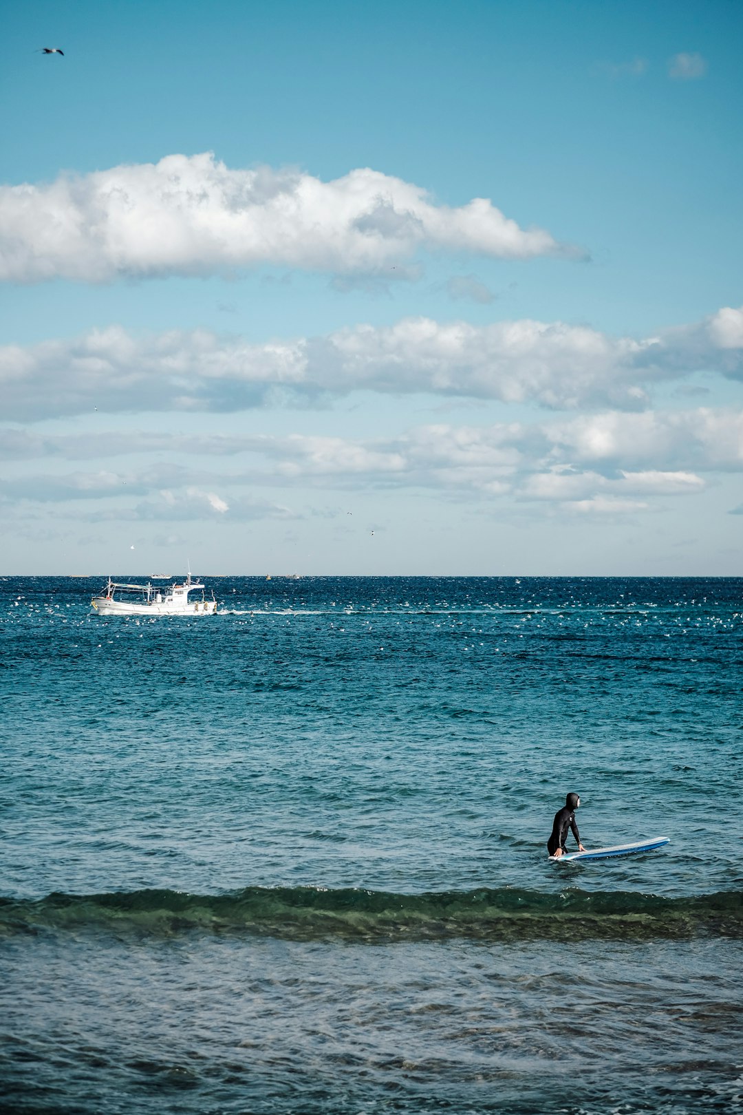 person with surfboard near boat at the ocean during day