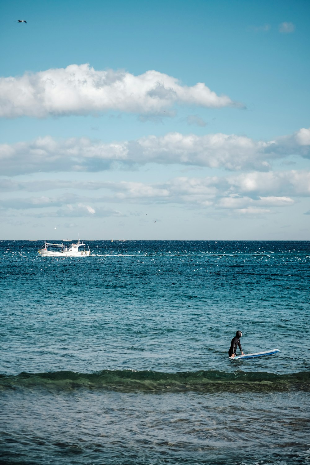 person with surfboard near boat at the ocean during day