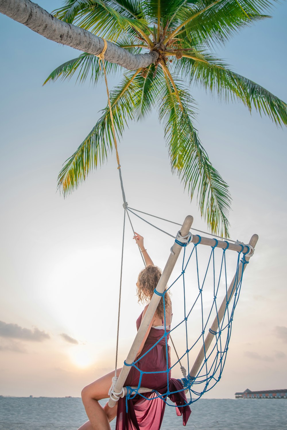 woman riding swing tied to a coconut tree on island during day