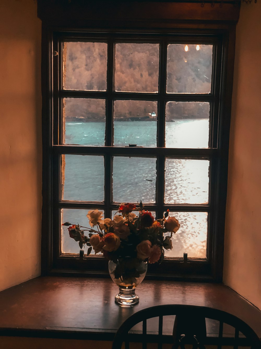white and red rose flowers in vase near closed window viewing body of water