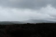 A moody landscape with rolling hills under a dramatic cloudy sky.