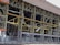 A large industrial building with a steel framework, featuring rust and wear. The structure includes multiple levels supported by metal beams, with exposed wiring and various construction materials scattered on the site. Safety barriers and fencing indicate an area under construction or repair.