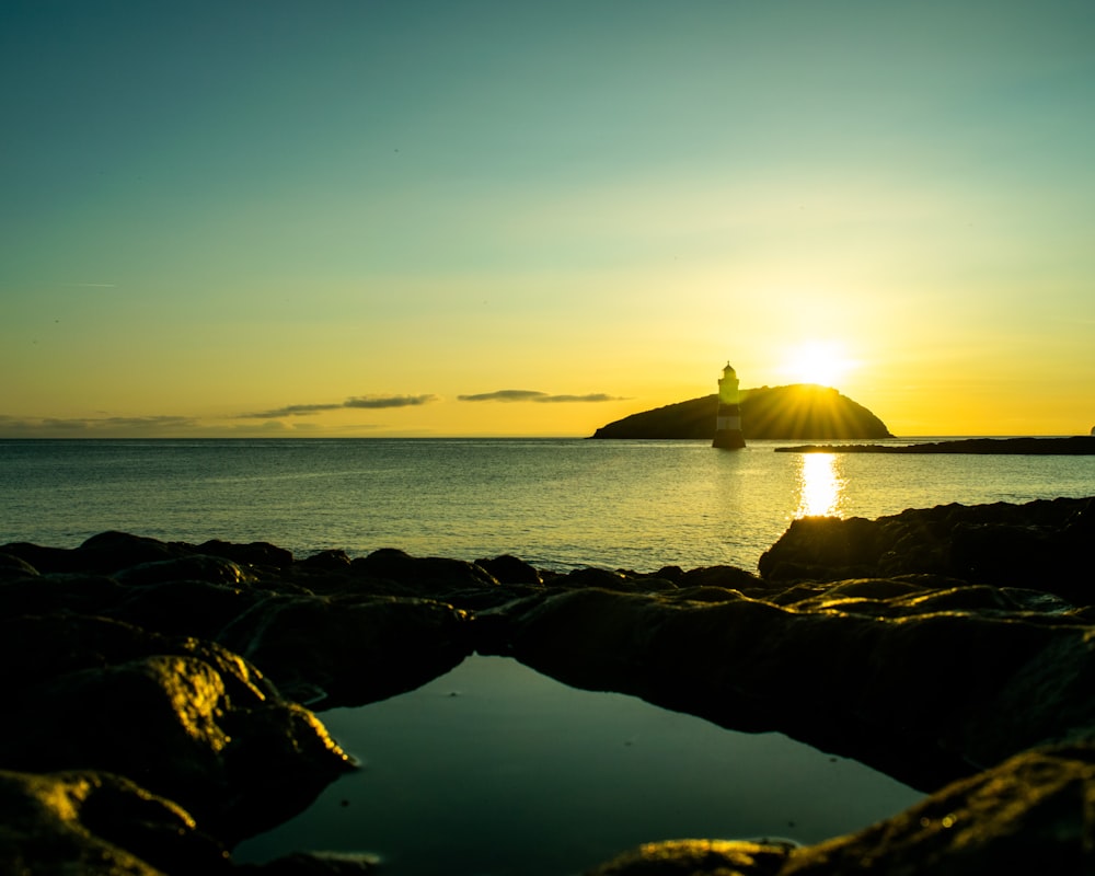 silhouette of rock formation on sea during sunset