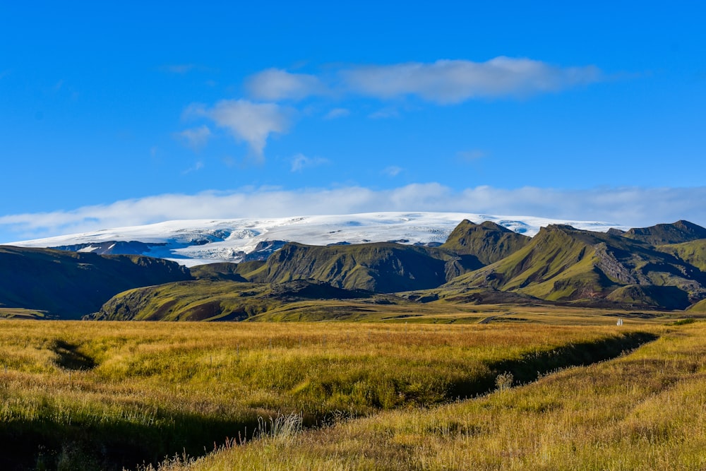 aerial photography of green field viewing mountain under blue and white sky