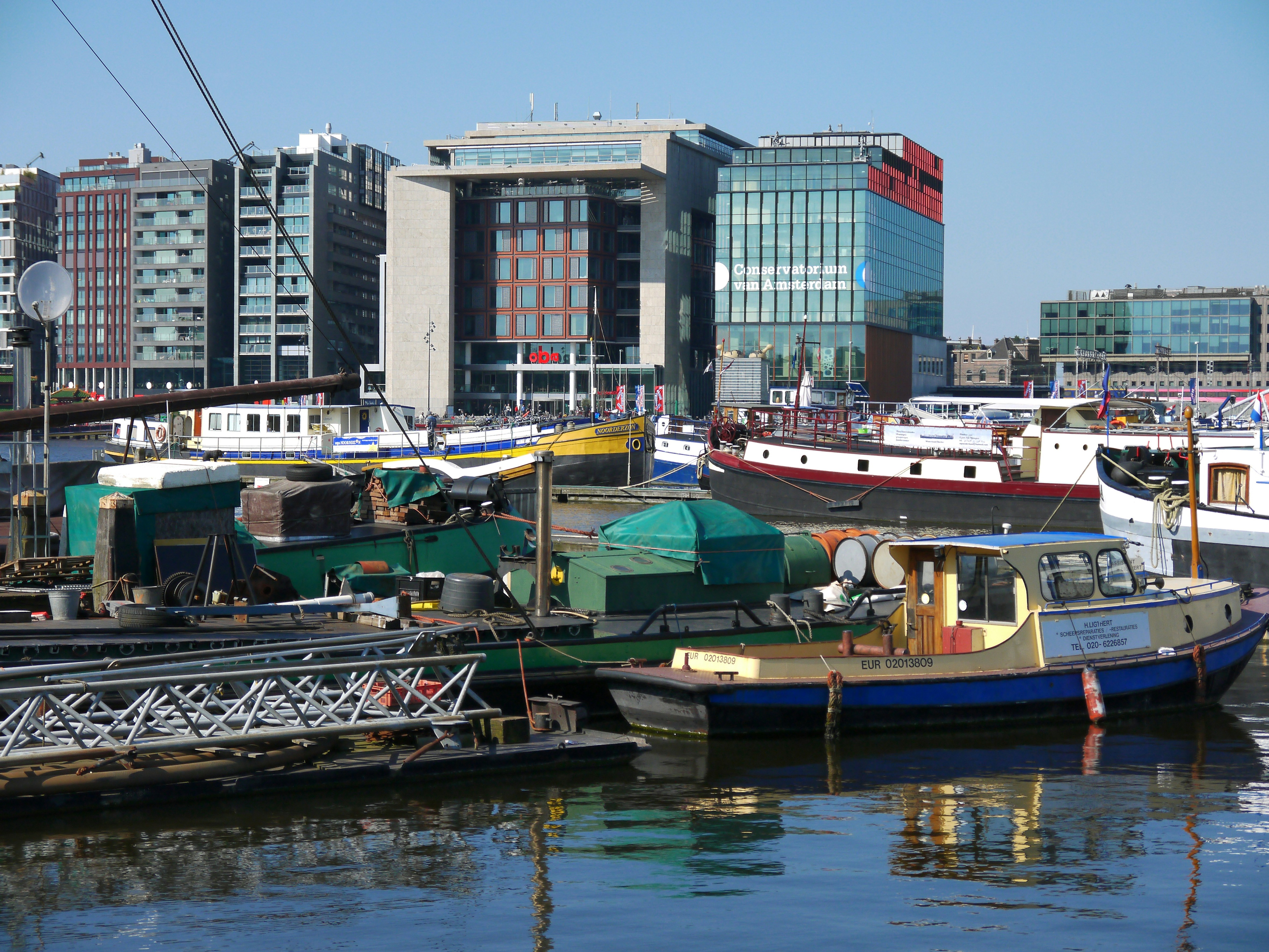 different boats on body of water near city with high-rise buildings during daytime, Photo of boats in the water, in front of modern city buildings inAmsterdam city. Free image of modern architecture facades of Oosterdokseiland, whit in front of the picture a floating collections of small boats and ships in the reflecting blue water. Street photography of big cities in The Netherlands by Fons Heijnsbroek, October 2016.