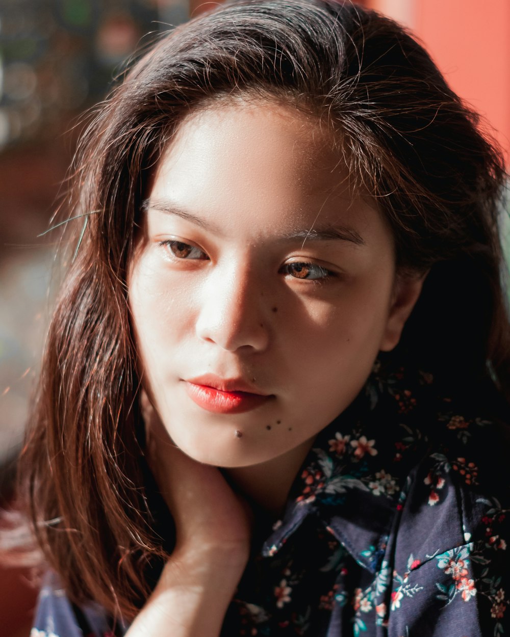 portrait photography of woman wearing blue and red floral collared top putting right hand on her neck