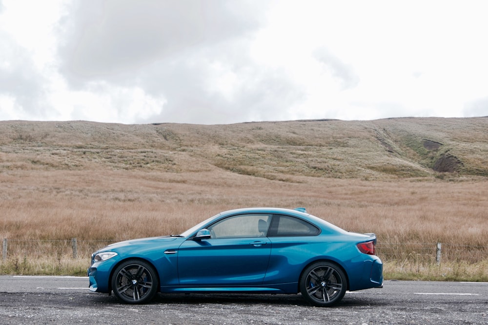 blue BMW coupe on road near empty field at daytime