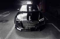 A sleek, dark gray luxury car reflecting light, parked in a minimalist, modern garage setting.