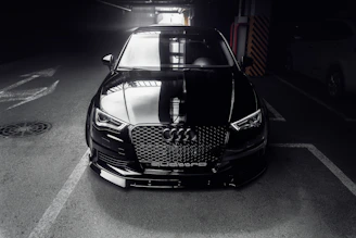 A sleek black luxury sports car parked in a dimly lit, elegant garage with soft shadows.