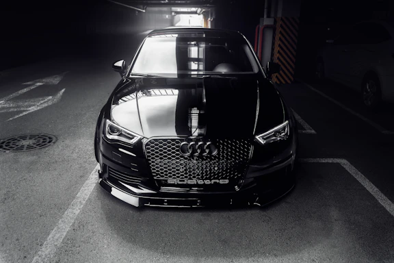 A sleek black luxury sports car parked in a dimly lit, elegant garage with soft shadows.