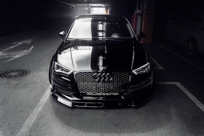 A sleek, dark gray luxury car reflecting light, parked in a minimalist, modern garage setting.