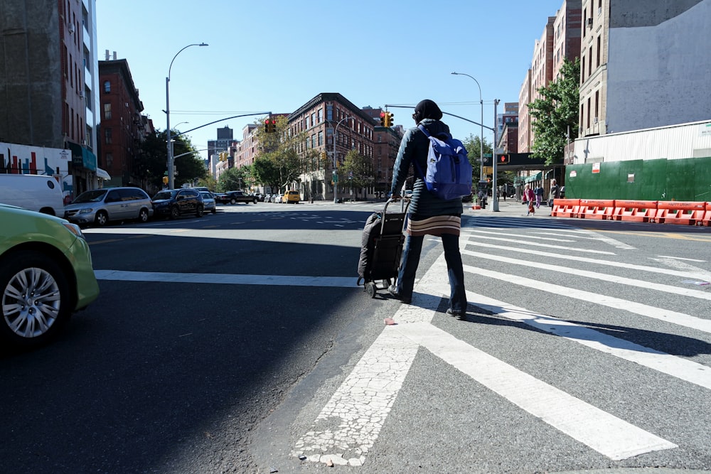 person walking on road while pushing luggage during daytime