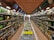 A supermarket aisle lined with shelves filled with a diverse selection of bottles and boxes, primarily alcoholic beverages. The ceiling is arched with a brick pattern and the floor is polished tile. At the far end of the aisle, there are people shopping.