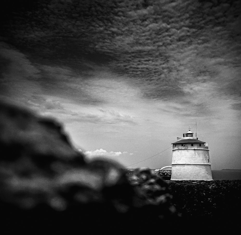 grayscale photography of a lighthouse under a cloudy sky