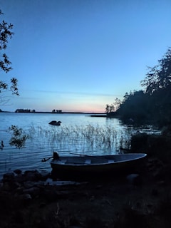 A peaceful lakeside scene at dusk, with mist rising and a single boat resting quietly.