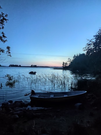 A peaceful lakeside scene at dusk, with mist rising and a single boat resting quietly.