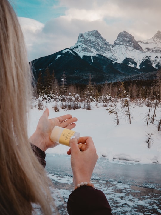 woman holding yellow and clear container while facing snow-covered field and mountains in The Three Sisters Canada