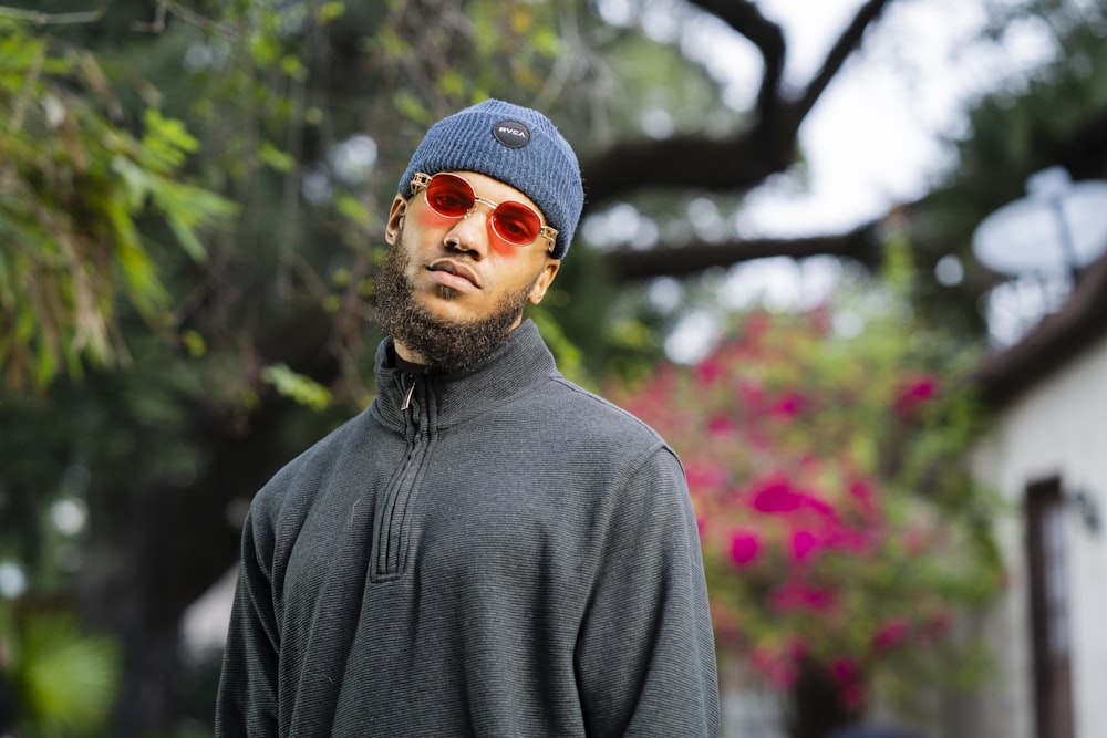 a man wearing a hat and sunglasses standing in front of a house