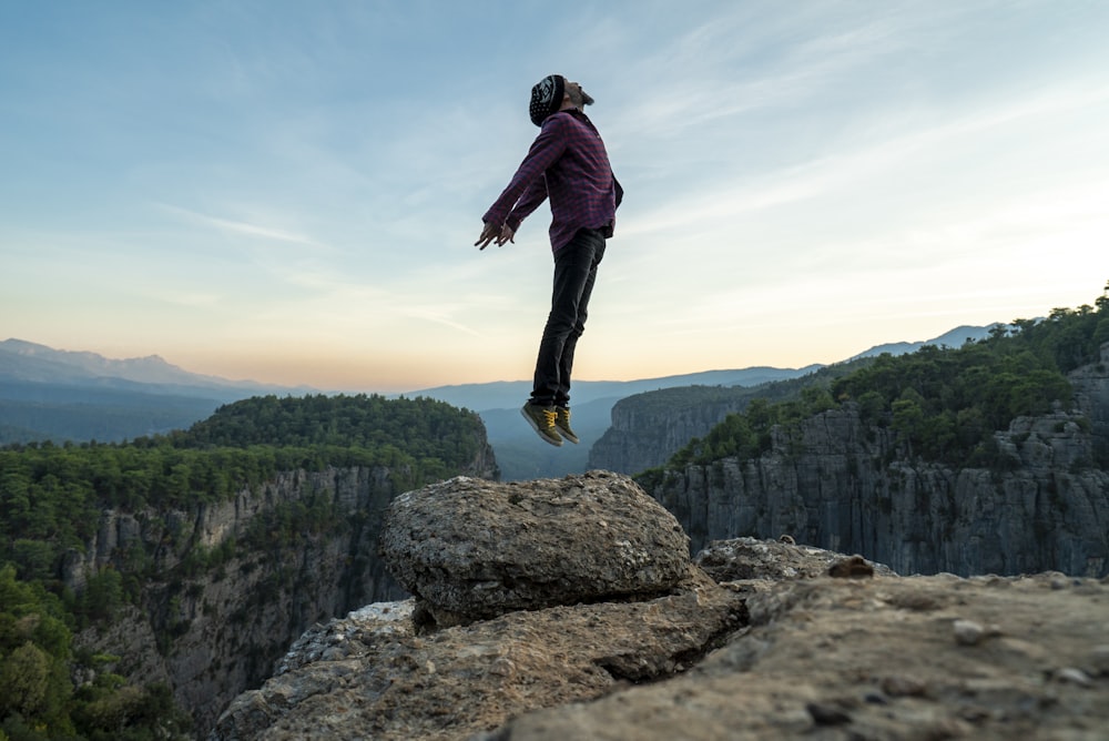 timelapse photo of person jumping above rock