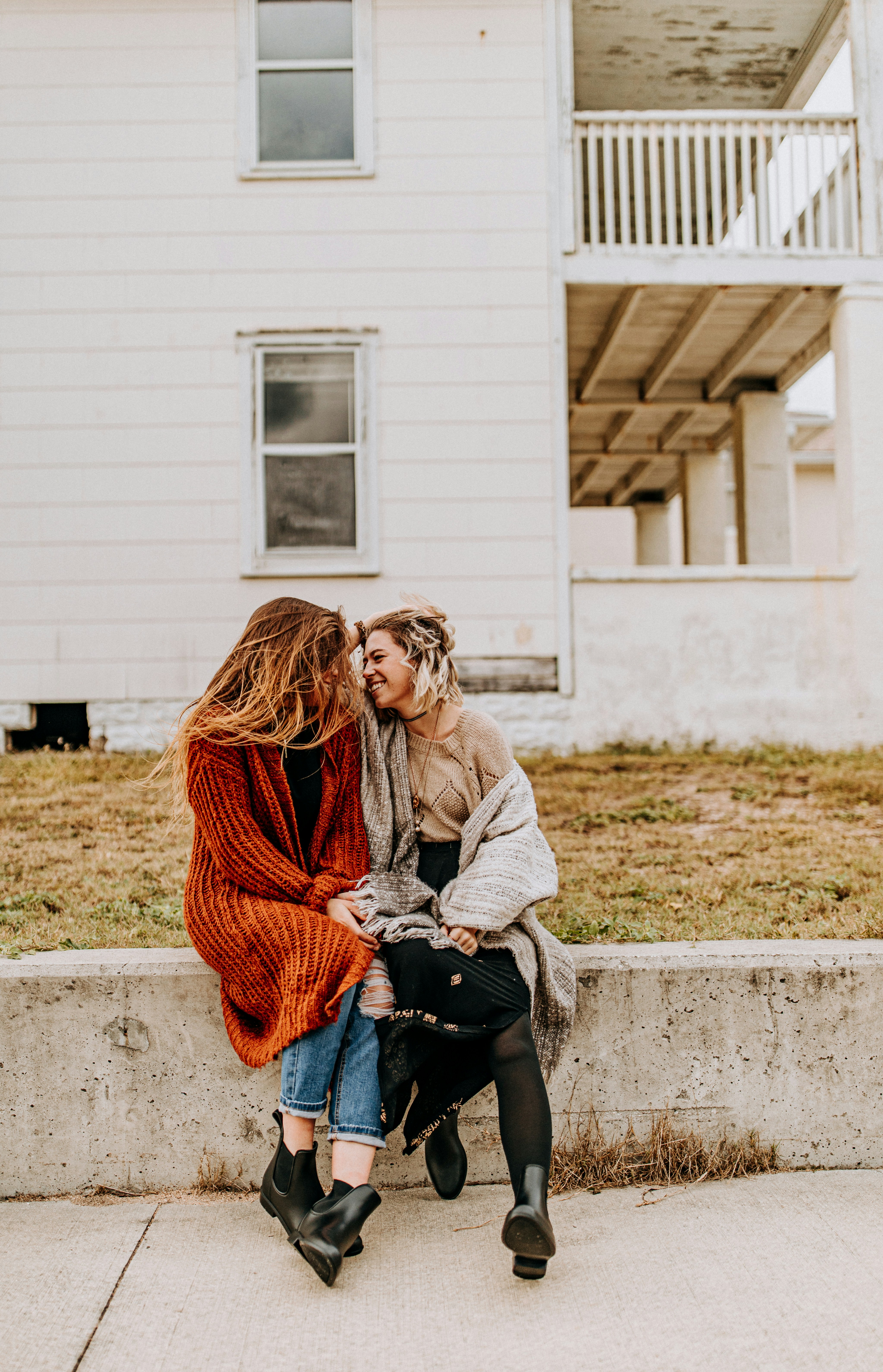 two women sitting and facing closely to each other in front of house during day