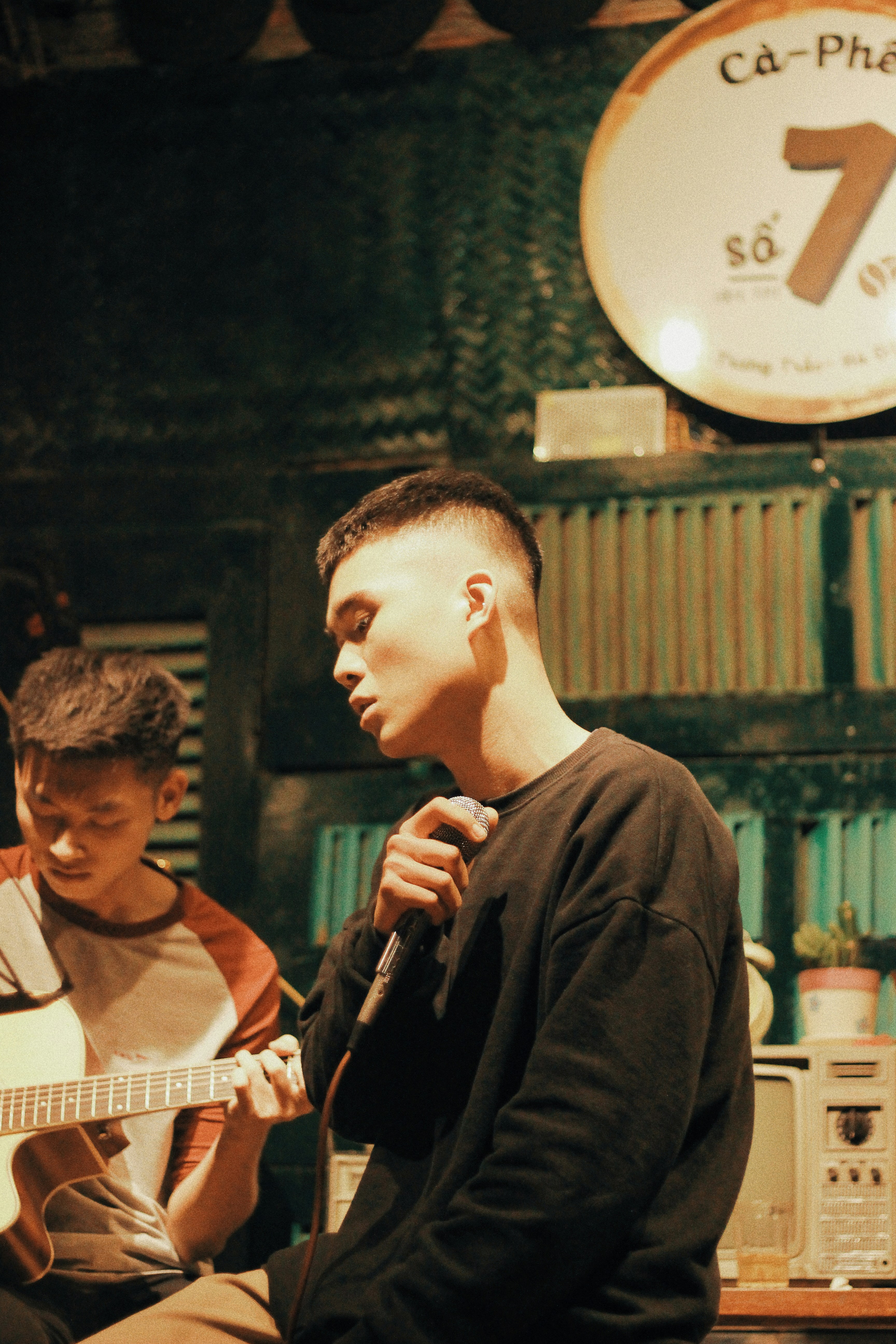 Pria mengenakan kemeja crew-neck hitam memegang mikrofon di samping pria bermain gitar