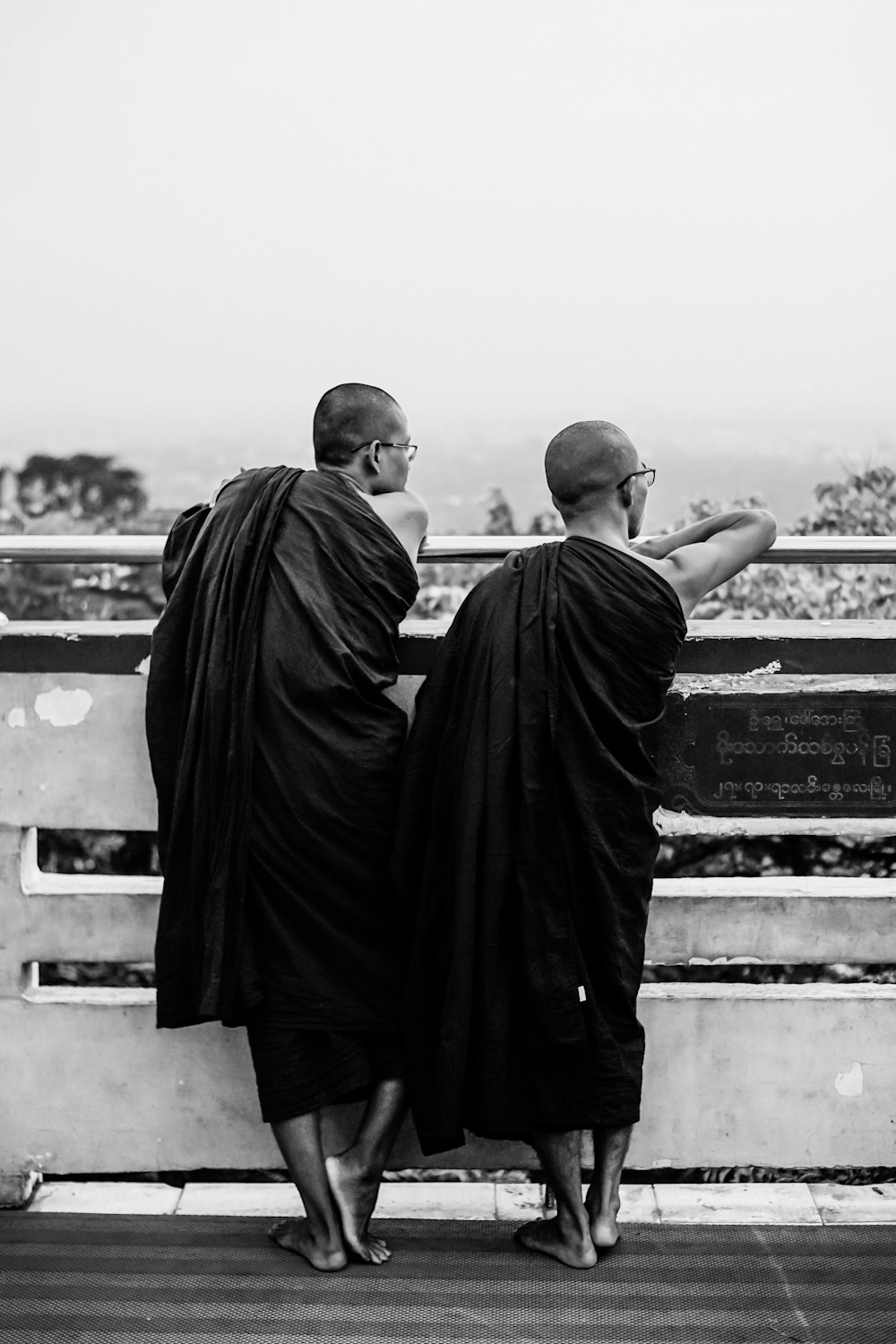 grayscale photography of two men standing while facing back on railings