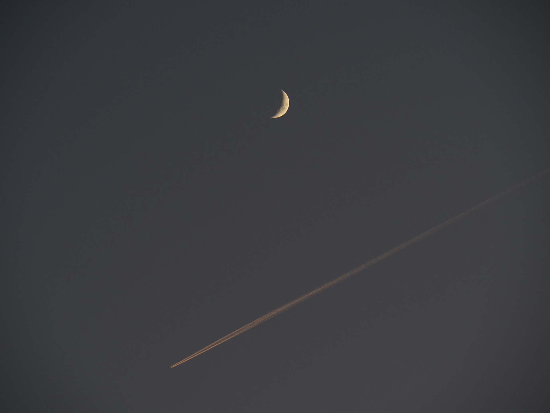 a plane flying in the sky with a half moon in the background