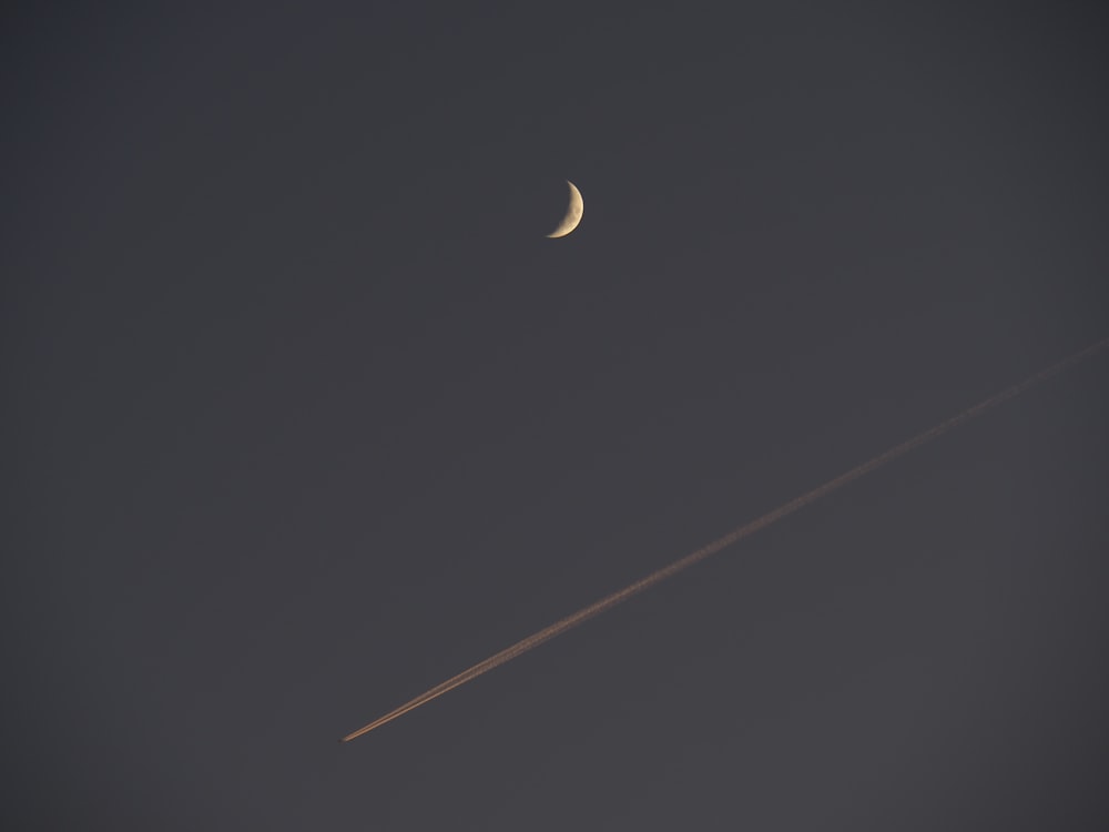 a plane flying in the sky with a half moon in the background