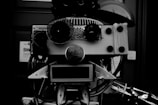 A robotic face crafted from various mechanical and electronic components, including speakers, wires, and metal parts, arranged in a way to resemble facial features.