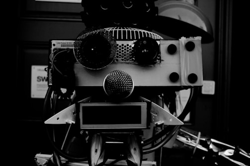 A robotic face crafted from various mechanical and electronic components, including speakers, wires, and metal parts, arranged in a way to resemble facial features.