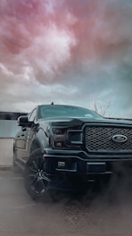A 2021 Peterbilt 389 truck parked beside a river under a cloudy sky, symbolizing strength and steady flow.