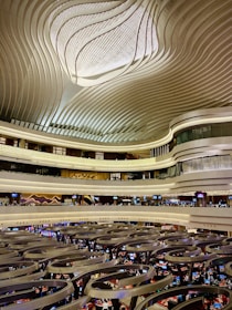 An architectural space with a large, intricately designed ceiling featuring wavy patterns. Multiple floors with balconies overlook a bustling gaming or trading floor with numerous people and electronic displays.
