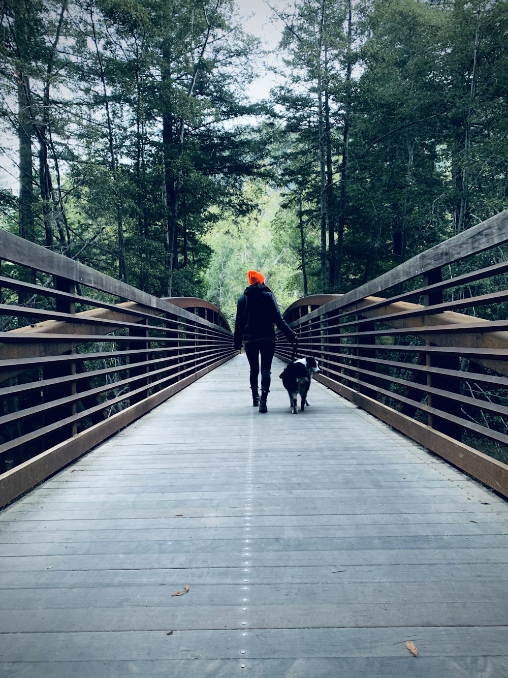 person in black jacket walking on wooden bridge