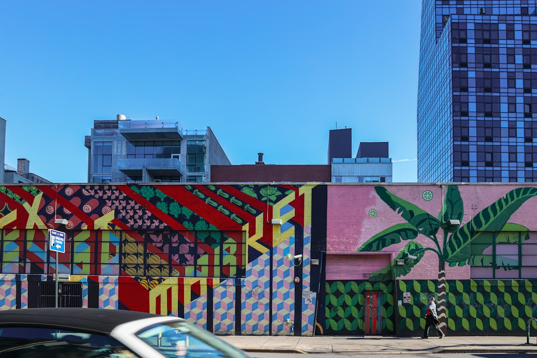 person walking beside building with murals during day, Palming Skies<p></figure>@ Lower Manhattan, Manhattan