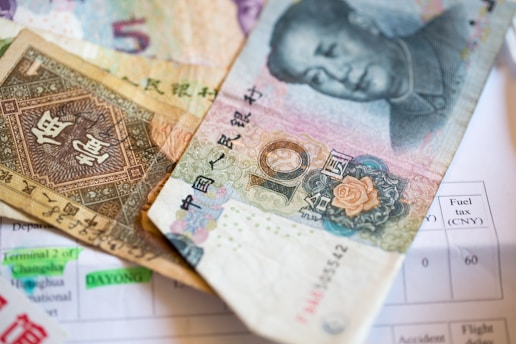 A close-up view of various Chinese currency notes placed on top of a document. Prominent features include traditional Chinese characters, intricate patterns, and a portrait of a notable individual on one of the notes. The document underneath has clearly visible English text and numerical values.