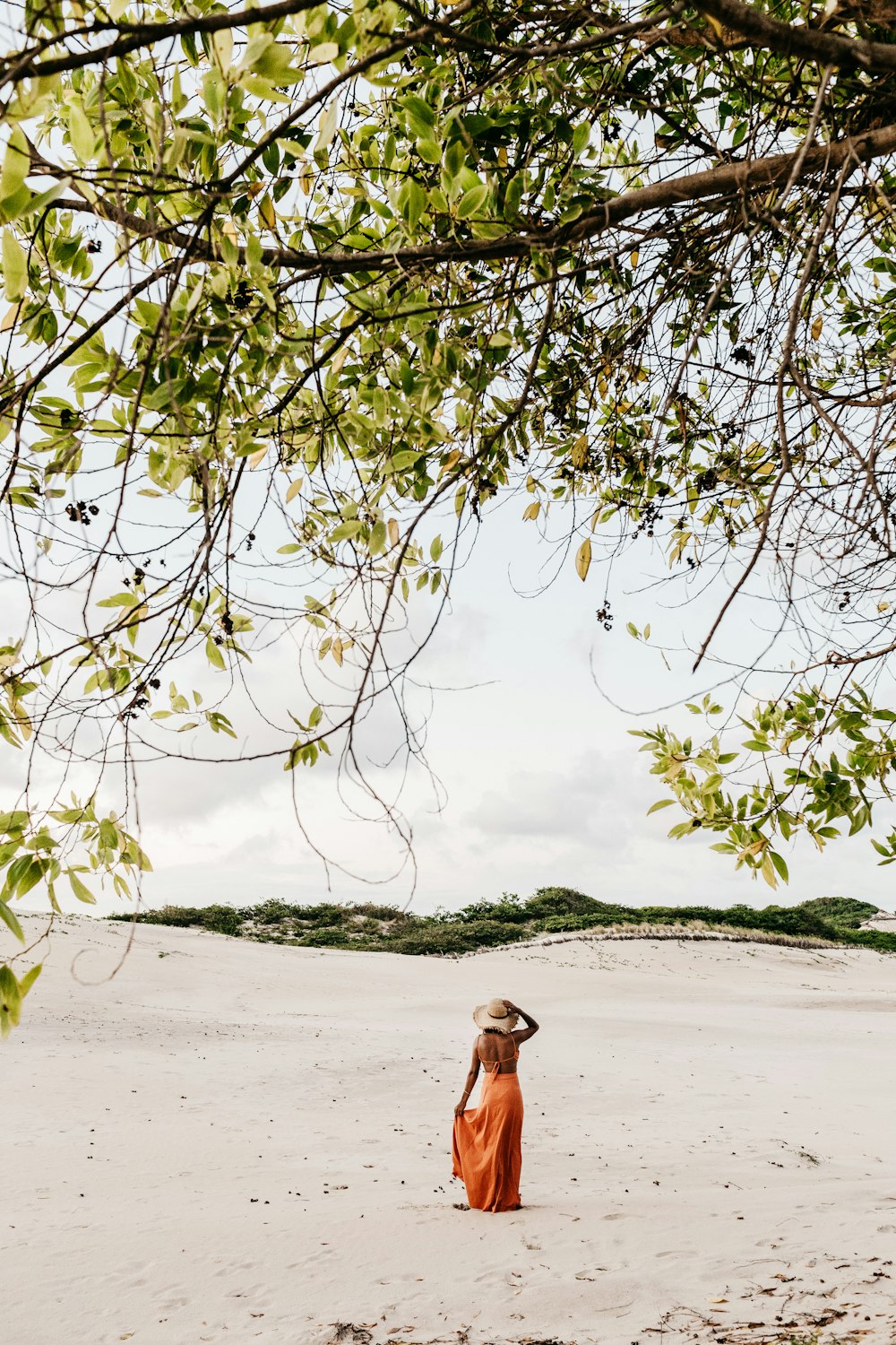 woman wearing orange dress standing on sand near tree during daytime