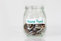 coins in clear glass jar with house fund sign