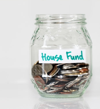 coins in clear glass jar with house fund sign